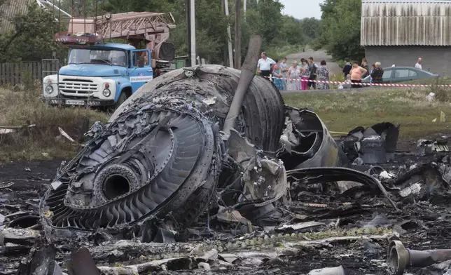 FILE - Local citizens, background, look at the site of a crashed Malaysia Airlines passenger plane near the village of Hrabove, Ukraine, on July 18, 2014. (AP Photo, File)