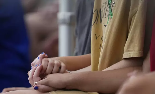 Attendees hold hands during a vigil for flooding victims at Tivy Antler Stadium on Wednesday, July 9, 2025, in Kerrville, Texas. (AP Photo/Ashley Landis)