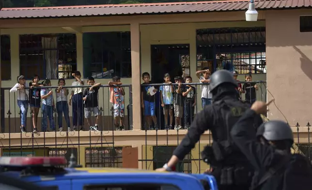 Students on their school's balcony watch a police convoy conducting an operation against alleged drug traffickers in La Mesilla, Guatemala, near the border with Mexico, Wednesday, July 30, 2025. (AP Photo/Moises Castillo)