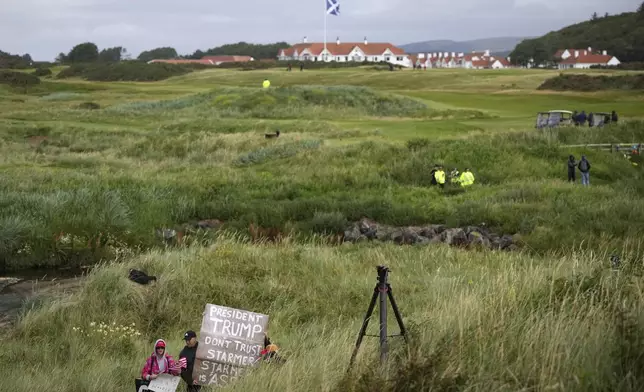 EDS NOTE: OBSCENITY - Trump supporters are watched by police and security forces as they hold signs near the Trump Turnberry golf course where President Donald Trump resides during his stay in Turnberry, Scotland, Sunday, July 27, 2025. (AP Photo/Alastair Grant)