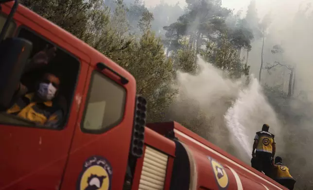Emergency responders with the Syrian Civil Defense, also known as the White Helmets, work to extinguish a wildfire in the town of Rabia, in the Latakia countryside, Syria, Saturday, July 5, 2025. (AP Photo/Ghaith Alsayed)