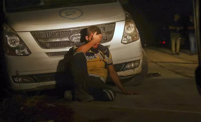 An emergency responder with the Syrian Civil Defense, known as the White Helmets, sits next to a car exhausted while working to extinguish a wildfire near the town of Rabia, in Syria's Latakia countryside, early Monday, July 7, 2025. (AP Photo/Ghaith Alsayed)
