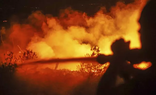 Emergency responders with the Syrian Civil Defense, known as the White Helmets, work to extinguish a wildfire near the town of Rabia, in Syria's Latakia countryside, early Monday, July 7, 2025. (AP Photo/Ghaith Alsayed)