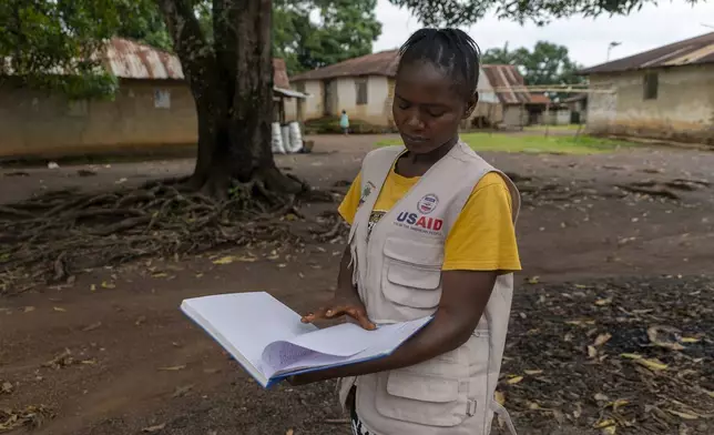 Alice Togbah, a community health worker, looks at a log of residents she provides health services to, in Bong County, Liberia, Saturday, June 14, 2025.(AP Photo/Annie Risemberg)