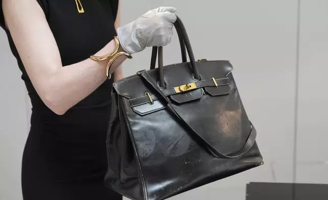 An auction officer carries the original Birkin bag created by Hermès for Jane Birkin in 1984, prior to its auction Thursday, July 10, 2025 in Paris. (AP Photo/Michel Euler)