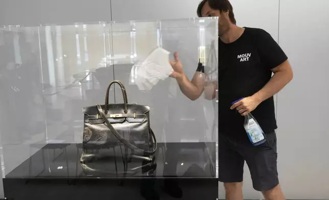 A man cleans a glass protecting the original Birkin bag created by Hermès for Jane Birkin in 1984 , prior to its auction Thursday, July 10, 2025 in Paris. (AP Photo/Michel Euler)
