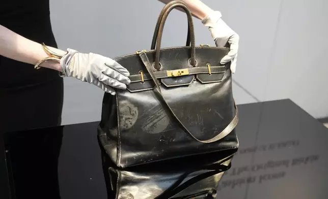An auction officer displays the original Birkin bag created by Hermès for Jane Birkin in 1984, prior to its auction Thursday, July 10, 2025 in Paris. (AP Photo/Michel Euler)