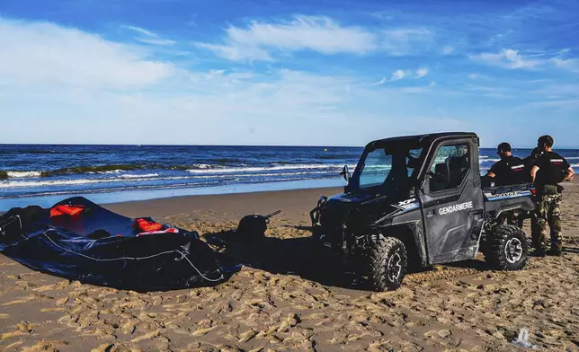 Police officers stand close to a ripped migrant inflatable dinghy lies on Ecault beach, northern France, Friday, July 4, 2025 northern France (AP Photo/Nicolas Garriga)