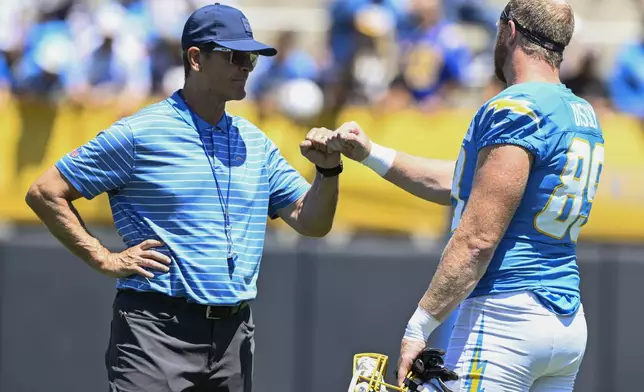 Los Angeles Chargers' head coach Jim Harbaugh, left, fist bumps tight end Will Dissly (89) during practice at the team's NFL football training camp, Wednesday, July 23, 2025, in San Diego. (AP Photo/Denis Poroy)