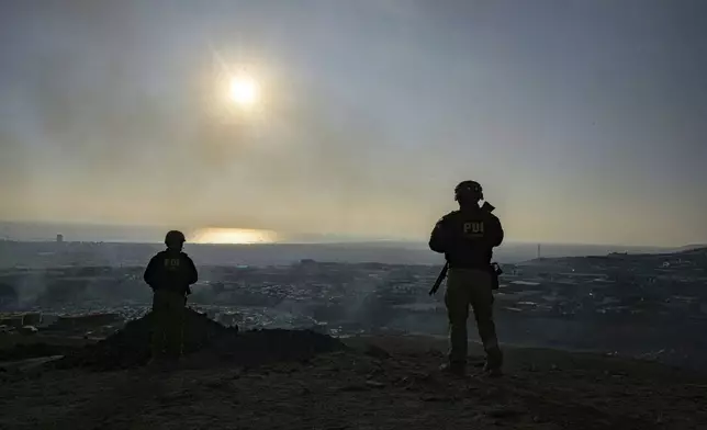 Bodyguards stand guard as prosecutor Mario Carrera surveys the shantytown of Cerro Chuño, a stronghold of Los Gallegos, the northern Chilean offshoot of the Tren de Aragua criminal gang, in Arica, Chile, Sunday, June 8, 2025. (AP Photo/Esteban Felix)