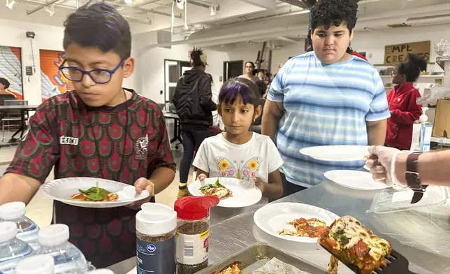 FILE - Attendees of the after school nutrition program, Milwaukee Public Library Snack Hack, line up to get a slice of pizza made from scratch, Nov. 19, 2024, in Milwaukee. (AP Photo/Devi Shastri, File)