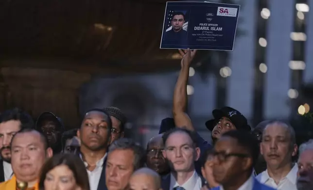 A man holds up a poster in memory of NYPD officer Didarul Islam during a vigil at Bryant Park for the people killed by a gunman at a Manhattan office building the day before, Tuesday, July 29, 2025, in New York. (AP Photo/Angelina Katsanis)
