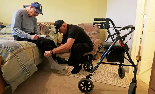 FILE - Caregiver Warren Manchess helping Paul Gregoline with his shoes and socks, in Noblesville, Ind., Nov. 27, 2013. (AP Photo/Darron Cummings, File)