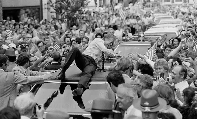 FILE - President Jimmy Carter leans across the roof of his car to shake hands along the parade route through Bardstown, Ky., on July 31, 1979. (AP Photo/Bob Daugherty, File)