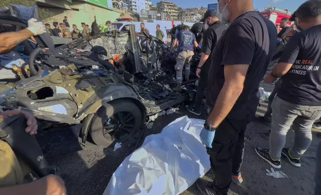 A Civil Defense worker stands over a body covered by a white bag that found inside a destroyed car that was hit in an Israeli drone strike in Khaldeh town, south of Beirut, Lebanon, Thursday, July 3, 2025. (AP Photo/Hussein Malla)