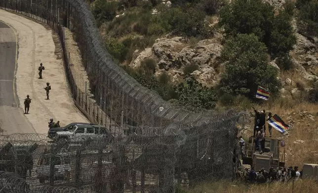 Israeli soldiers stand guard as Syrian Druze protest near the Israeli-Syrian border, as seen from the town of Majdal Shams in the Israeli-controlled Golan Heights, Wednesday, July 16, 2025, amid ongoing clashes between Syrian government forces and Druze armed groups in the southern Syrian city of Sweida. (AP Photo/Leo Correa)