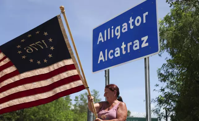 Rana Mourer waves an American flag outside of the migrant detention facility dubbed "Alligator Alcatraz," at the Dade-Collier Training and Transition facility, Saturday, July 12, 2025 in Ochopee, Fla. (AP Photo/Alexandra Rodriguez)