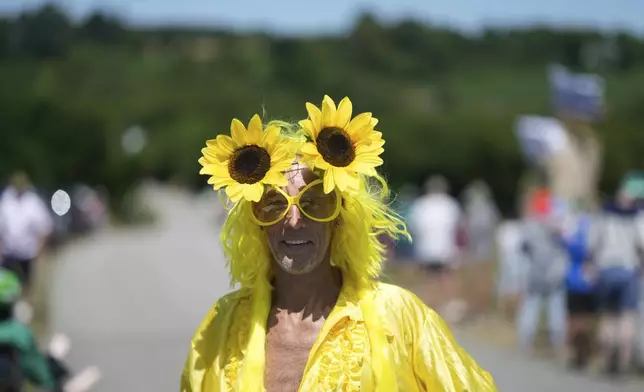 A spectator with sunflowers on the head poses during the seventh stage of the Tour de France cycling race over 197 kilometers (122.4 miles) with start in Saint-Malo and finish in Mur-de-Bretagne Guerledan, France, Friday, July 11, 2025. (AP Photo/Mosa'ab Elshamy)