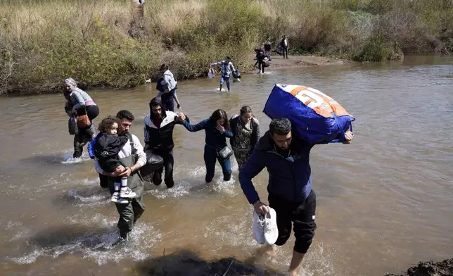 FILE - Syrian Alawite families who fled the clashes in Syria carry their luggage as they cross a river marking the border between Syria and northern Lebanon near the village of Heker al-Daher in Akkar province, Lebanon, March 11, 2025. (AP Photo/Hussein Malla, File)