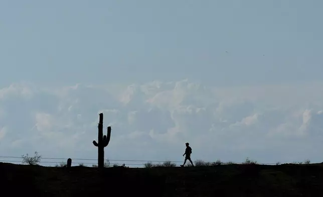 Storm clouds form in the distance as a hiker walks along a path in South Mountain Park Wednesday, June 4, 2025, in Phoenix. (AP Photo/Ross D. Franklin)