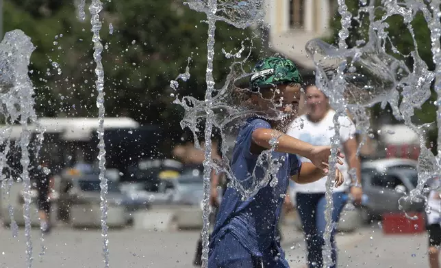 A boy plays in a fountain during hot weather in Kosovo's capital Pristina on Thursday, July 3, 2025. (AP Photo/Visar Kryeziu)