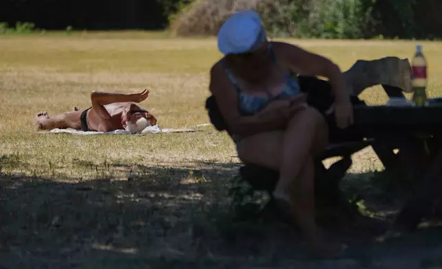 A person sits in the shade while another lies sunbathing during a hot summer day in Belgrade, Serbia, Thursday, July 3, 2025. (AP Photo/Darko Vojinovic)