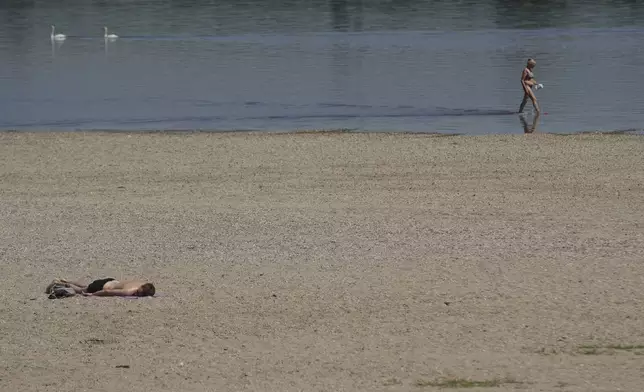 A woman wades through the Danube river as a man lies sunbathing on the bank during a hot summer day in Belgrade, Serbia, Thursday, July 3, 2025. (AP Photo/Darko Vojinovic)