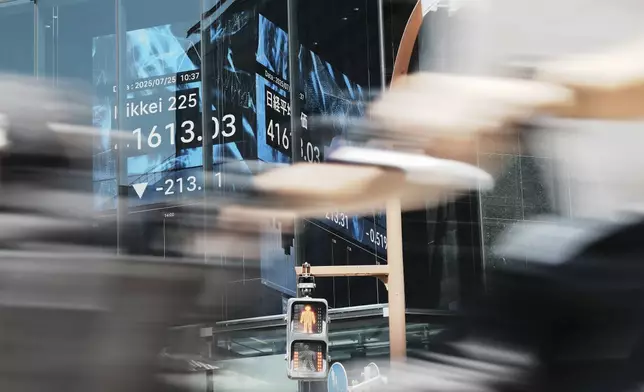 A person rides a bicycle past an electronic stock board showing Japan's Nikkei index at a securities firm Friday, July 25, 2025, in Tokyo. (AP Photo/Eugene Hoshiko)