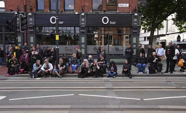 Fans gather near the Black Sabbath Bridge bench on Broad Street ahead of the funeral procession for Black Sabbath frontman Ozzy Osbourne, in Birmingham, England, Wednesday July 30, 2025. (Jacob King/PA via AP)