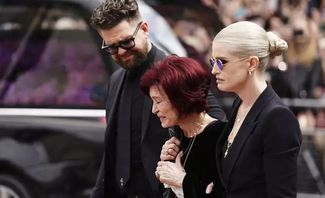 The family of Ozzy Osbourne from left, Jack Osbourne, Sharon Osbourne and Kelly Osbourne lay flowers and view the flowers left at the Black Sabbath Bridge bench on Broad Street in memory of Black Sabbath frontman Ozzy Osbourne ahead of the funeral procession, in Birmingham, England, Wednesday July 30, 2025. (Jacob King/PA via AP)