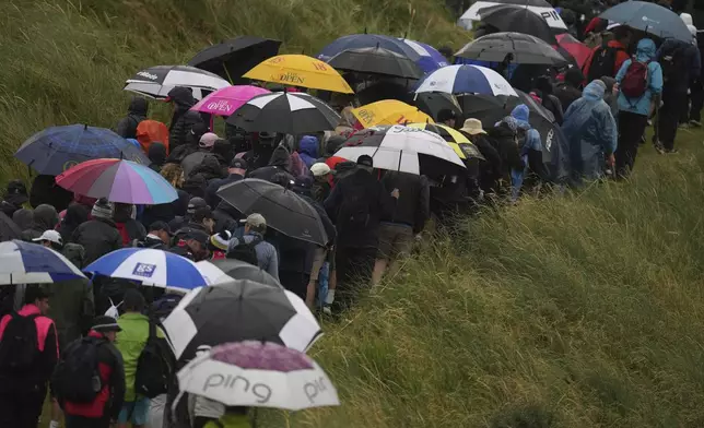 Spectators walks along the 7th fairway under umbrellas as heavy rain falls during the first round of the British Open golf championship at the Royal Portrush Golf Club, Northern Ireland, Thursday, July 17, 2025. (AP Photo/Francisco Seco)