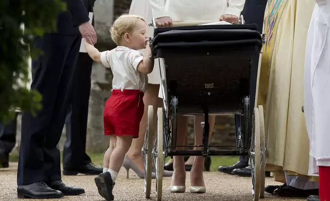 Britain's Prince George gets up on tiptoes to peek into the pram of Princess Charlotte, flanked by his parents, Prince William and Kate, the Duchess of Cambridge, as they leave after Charlotte's Christening at St. Mary Magdalene Church in Sandringham, England, July 5, 2015. (AP Photo/Matt Dunham, File)