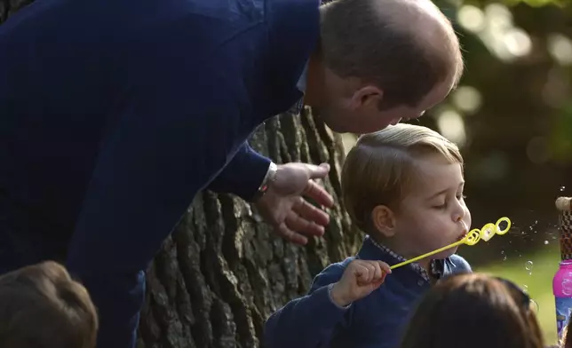 Prince George plays with bubbles as his father, Britain's Prince William, the Duke of Cambridge, watches during a children's tea party at Government House in Victoria, British Columbia, Sept. 29, 2016. (Jonathan Hayward/The Canadian Press via AP, File)
