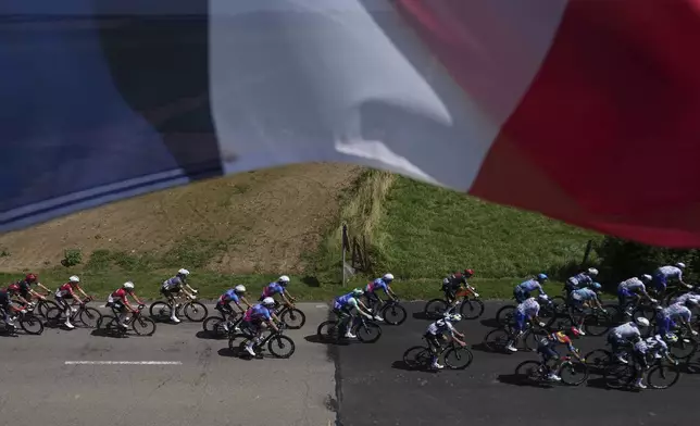 The pack rides under a French flag during the fourth stage of the Tour de France cycling race over 172.2 kilometers (107 miles) with start in Amiens and finish in Rouen, France, Tuesday, July 8, 2025. (AP Photo/Thibault Camus)