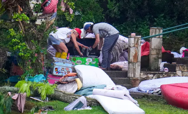 People look through belongings on a camp trunk at Camp Mystic along the banks of the Guadalupe River after a flash flood swept through the area Sunday, July 6, 2025, in Hunt, Texas. (AP Photo/Julio Cortez)