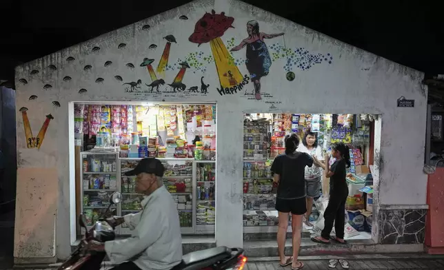 People are seen outside a grocery store whose facade is painted with a UFO and alien-themed mural, at a neighborhood colloquially known as a "UFO Village" in Yogyakarta, Indonesia, Friday, July 25, 2025. (AP Photo/Dita Alangkara)