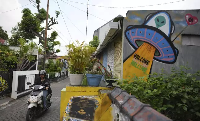 A motorist ride her motorbike past a UFO and alien-themed mural, at a neighborhood colloquially known as a "UFO Village" in Yogyakarta, Indonesia, Thursday, July 24, 2025. (AP Photo/Dita Alangkara)