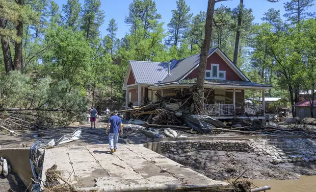 Residents of the town of Ruidoso, N.M., walk back to their neighborhood to find what's left of their homes a day after major flooding washed away properties leaving streets clogged with mud and debris, along the Rio Ruidoso, Wednesday, July 9, 2025, in Ruidoso, N.M. (AP Photo/Roberto E. Rosales)