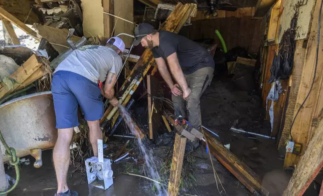 Wes Schenki, left and Neal Clawson work to shut off exposed water pipes in a cabin situated along the Rio Ruidoso Wednesday morning, July 9, 2025, in Ruidoso, N.M., after the town was hit with major flooding the day before. (AP Photo/Roberto E. Rosales)