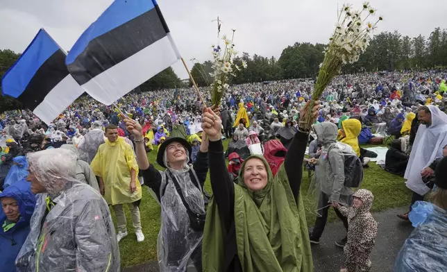 Spectators wave Estonian flags and bouquets of flowers during the song festival, part of the "Iseoma" Song and Dance Celebration, at the Song Festival Grounds in Tallinn, Estonia, Sunday, July 6, 2025. (AP Photo/Sergei Grits)