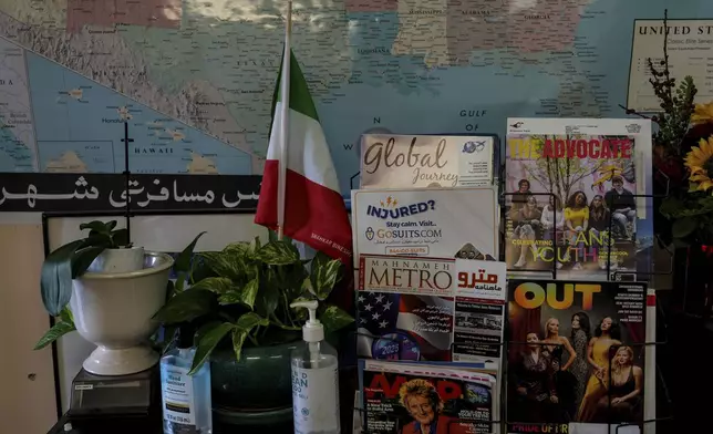 An Iranian flag is seen next to a magazine rack at Shahrzad Tahouri's travel agency in the "Tehrangeles" neighborhood of Los Angeles Tuesday, June 24, 2025. (AP Photo/Jae C. Hong)