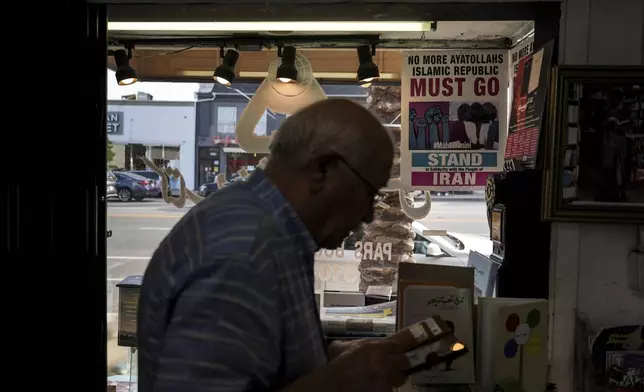 Sam Beykzadeh works in his bookstore in the "Tehrangeles" neighborhood of Los Angeles Tuesday, June 24, 2025, as a poster in the window calls for regime change in Iran. (AP Photo/Jae C. Hong)