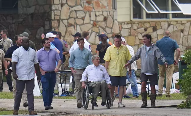 Texas Gov. Greg Abbott, center, tours Camp Mystic along the banks of the Guadalupe River after a flash flood swept through the area Saturday, July 5, 2025, in Hunt, Texas. (AP Photo/Julio Cortez)