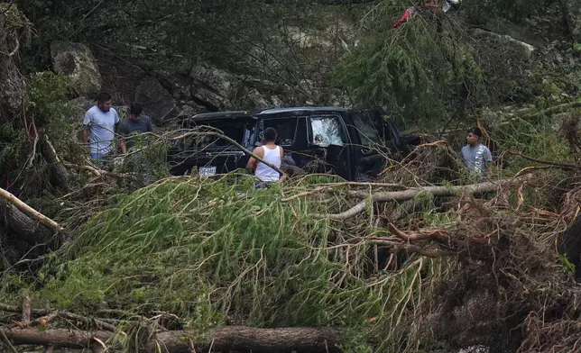 Men inspect a vehicle that was washed along the Guadalupe River near Camp Mystic after a flash flood swept through the area Saturday, July 5, 2025, in Hunt, Texas. (AP Photo/Julio Cortez)
