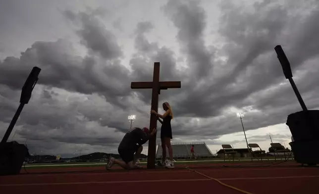 Dan Beazley, of Michigan, left, reacts as he holds a large cross with Abigail Smithson during a vigil for flooding victims at Tivy Antler Stadium on Wednesday, July 9, 2025, in Kerrville, Texas. (AP Photo/Gerald Herbert)