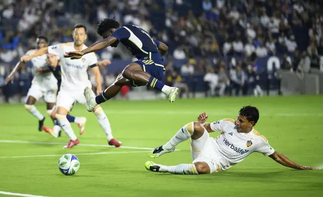 Vancouver Whitecaps forward Emmanuel Sabbi, center, jumps over Los Angeles Galaxy midfielder Edwin Cerrillo, right, during the first half of an MLS soccer match Friday, July 4, 2025, in Carson, Calif. (AP Photo/William Liang)