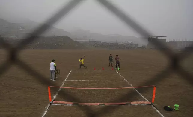 Tennis coach Delfin Barrial, left, teaches children how to hold a racket during a class in the Jicamarca neighborhood on the outskirts of Lima, Peru, Sunday, July 6, 2025. (AP Photo/Guadalupe Pardo)