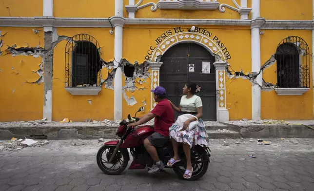 A couple ride past a community hall damaged as a result of dozens of earthquakes and aftershocks recorded in a matter of hours, in Santa Maria de Jesus, Guatemala, Wednesday, July 9, 2025. (AP Photo/Moises Castillo)