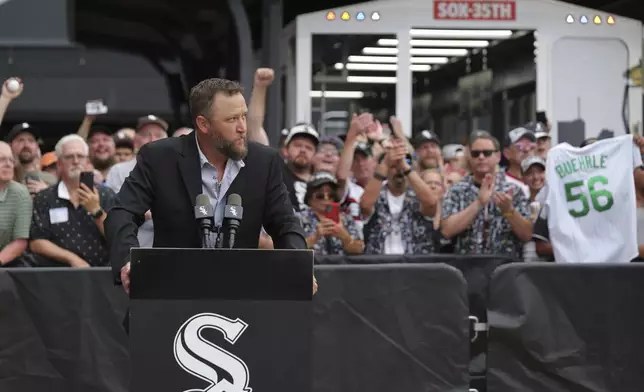 Former Chicago White Sox pitcher Mark Buehrle speaks at a lectern after the team unveiled a statue of him as they celebrate their 2005 World Series-winning team before a baseball game against the Cleveland Guardians, Friday, July 11, 2025, in Chicago. (AP Photo/Melissa Tamez)