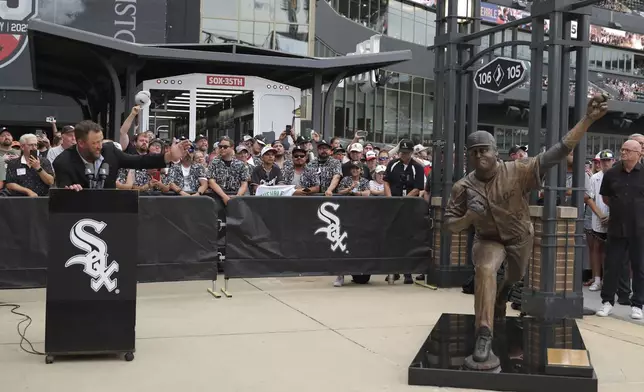 Former Chicago White Sox pitcher Mark Buehrle, left, speaks at a lectern after the team unveiled a statue of him as they celebrate their 2005 World Series-winning team before a baseball game against the Cleveland Guardians, Friday, July 11, 2025, in Chicago. (AP Photo/Melissa Tamez)